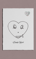 Heart-shaped face drawing with eyes and a mouth on a white card, with a heart-shaped object attached, on a beige background.